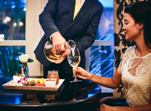 Man pouring wine into woman's glass, olive and nut tray on the table 