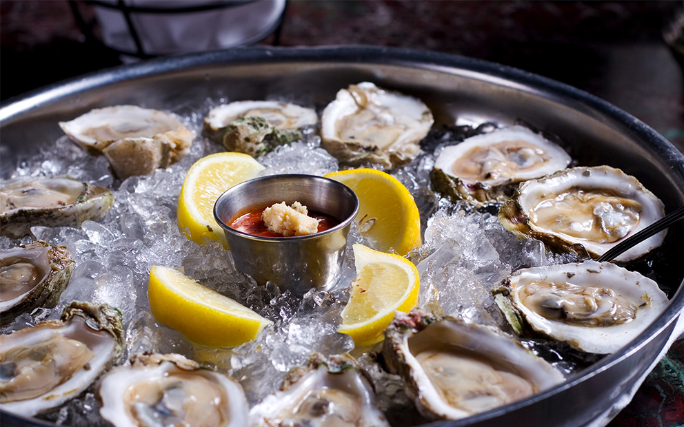 Large platter of clams on ice with lemon wedges in the center