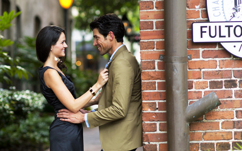 Man leaning against brick wall as he holds woman by the waist