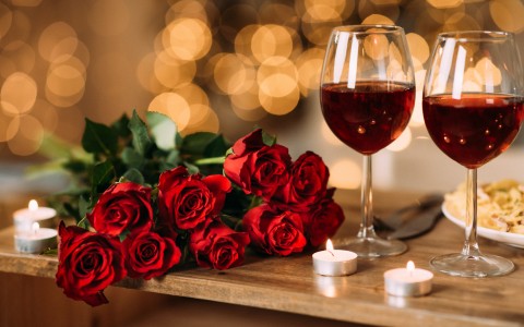 red roses and two glasses of red wine with candles 