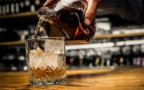 bartender pouring whiskey in rocks glass