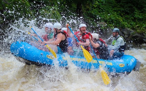 family white water rafting in blue raft with red and green life jackets