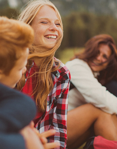 girl with blonde hair sitting outside next to mother and brother laughing
