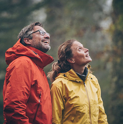 man with red rain coat and woman with yellow rain coat outside in the woods exploring 