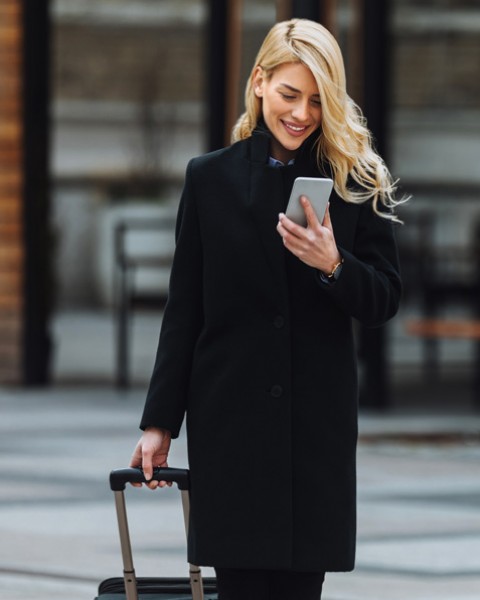 elegant woman carrying her luggage while she is walking and looking at her mobile