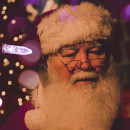 Santa Claus with white beard and red and white hat surrounded by Christmas Lights