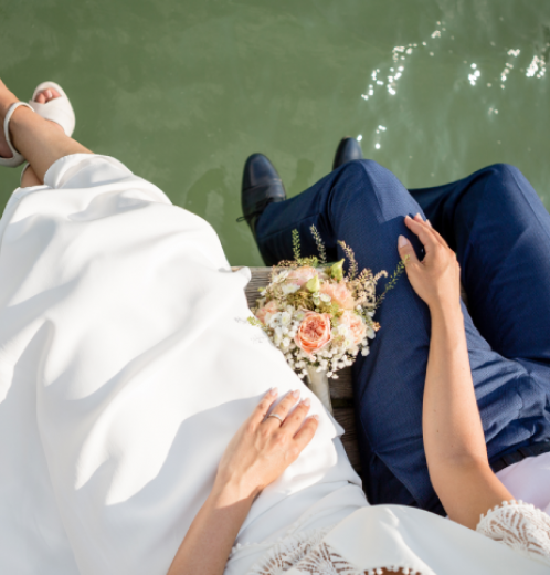 bride and groom sitting on wooden ledge over lake