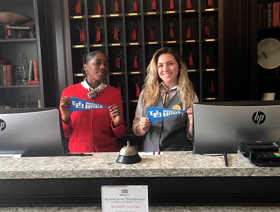 Two women working at the check in counter holding small university flags