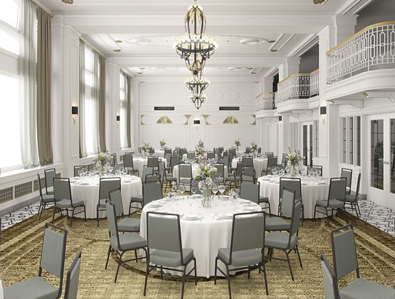 Large event area set up for dining with many round tables set with white tablecloths and gray chairs
