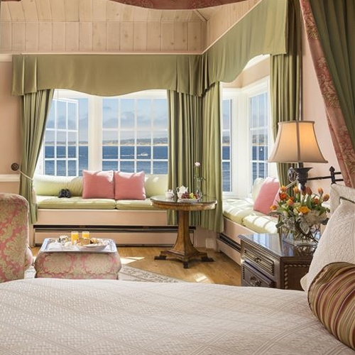 guest room with light green window seats and pink accent pillows with a view of a dresser lamp and the bed 