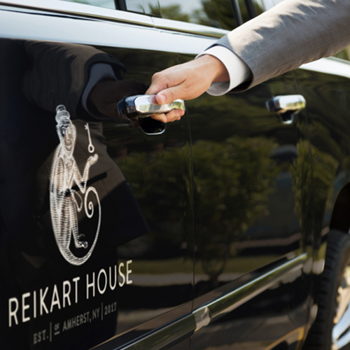 close up of a persons hand on a car door with the reikart house logo