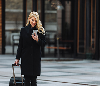 woman walking with luggage and looking at her cell phone