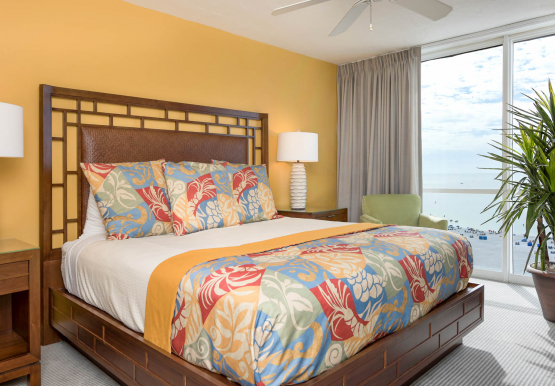 King bedroom with tropical patterned bedding, wooden furniture & beach view window