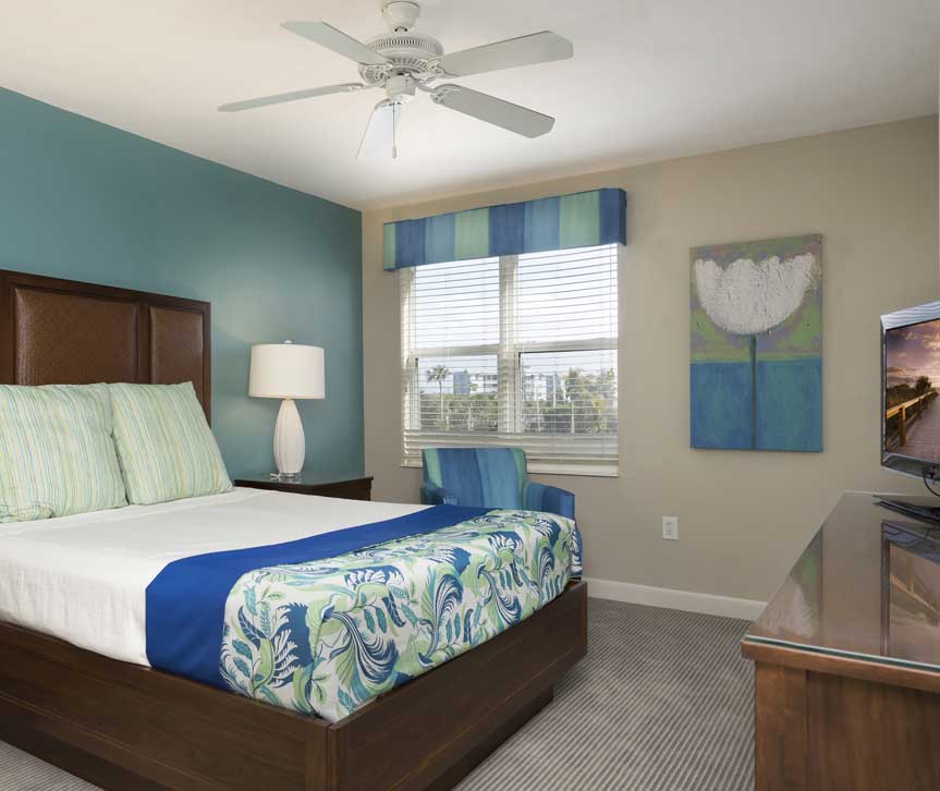 Room with queen bed, wooden dresser with tv, blue accent decor & window
