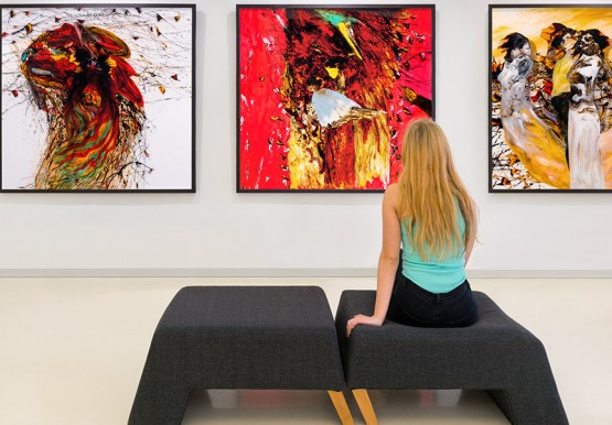 Girl sitting on chair at museum in front of three paintings