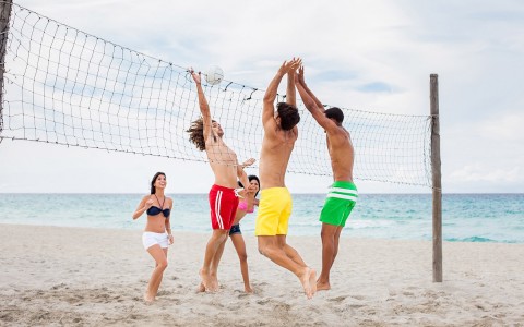 Group of friends playing volleyball on beach 