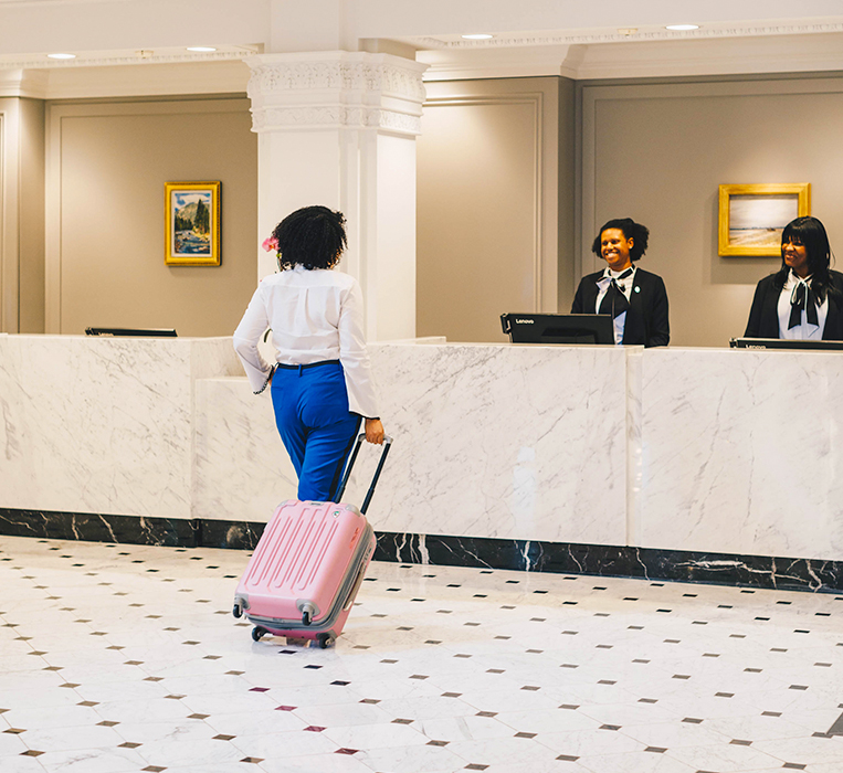 a woman with a pink suitcase walking up to reception desk