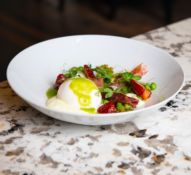 buratta in a bowl with fruits and meats around it
