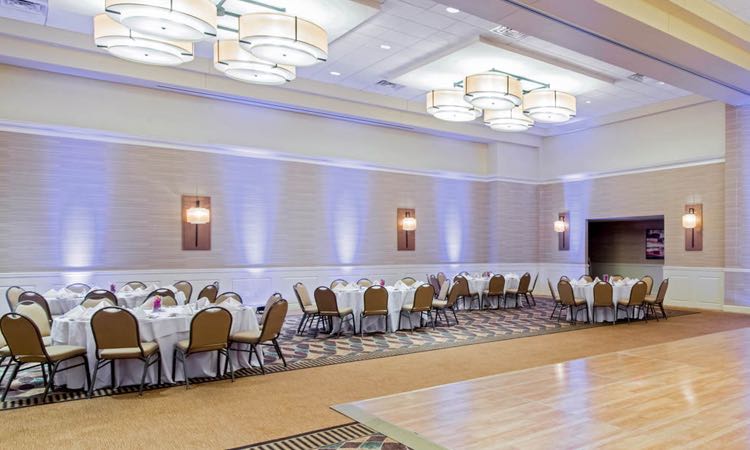 Large room with round tables set for reception next to wooden dancefloor