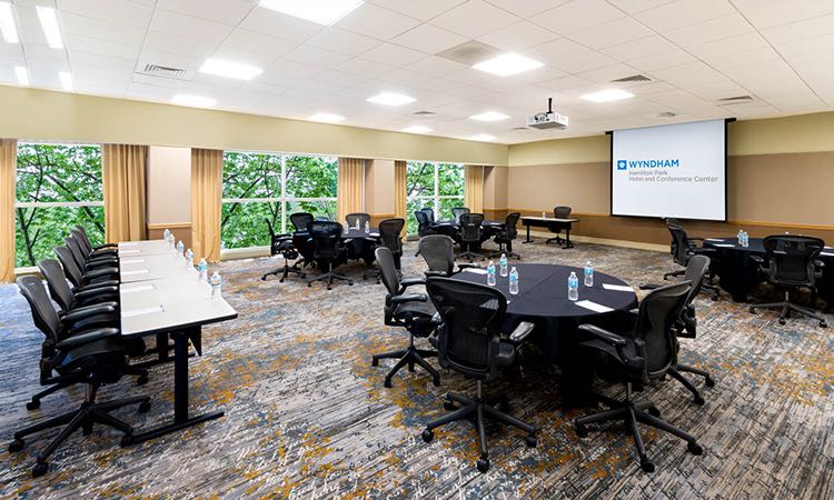 Boardroom with one long rectangular table & other circular tables facing projection screen