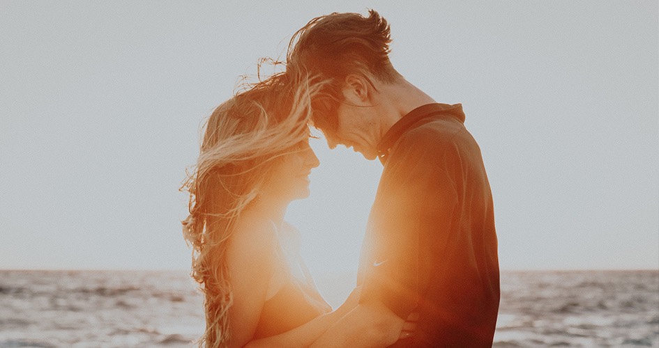 man and woman embracing by the ocean at sunset