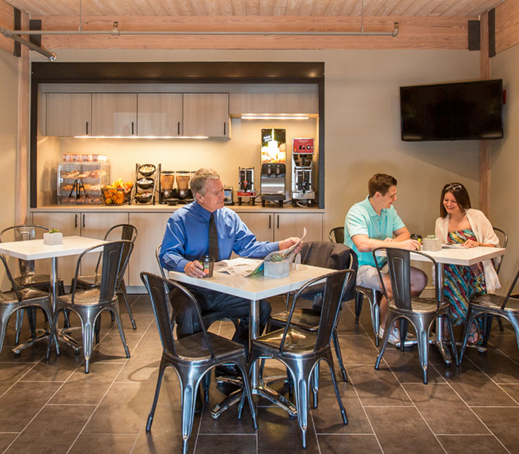 People eating in the hotel breakfast area with a food bar and table seating