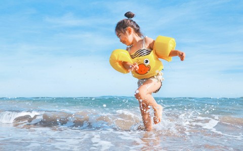 little girl playing in ocean with yellow duckie floaties