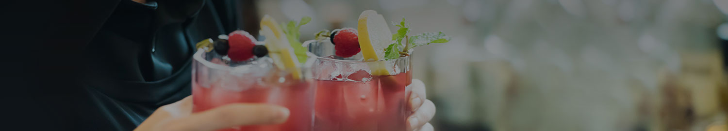Close up of someone holding two fruity cocktail drinks garnished with lemons, raspberries, blueberries, and mint