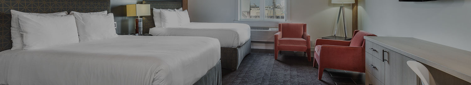 Two beds with a dresser and cushioned chairs in the corner of the room