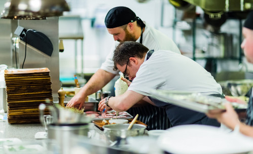 chefs at harvest table working over a plate of food at the expediting line