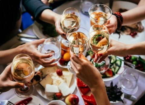 group of people clinking glasses of white wine over a table of food