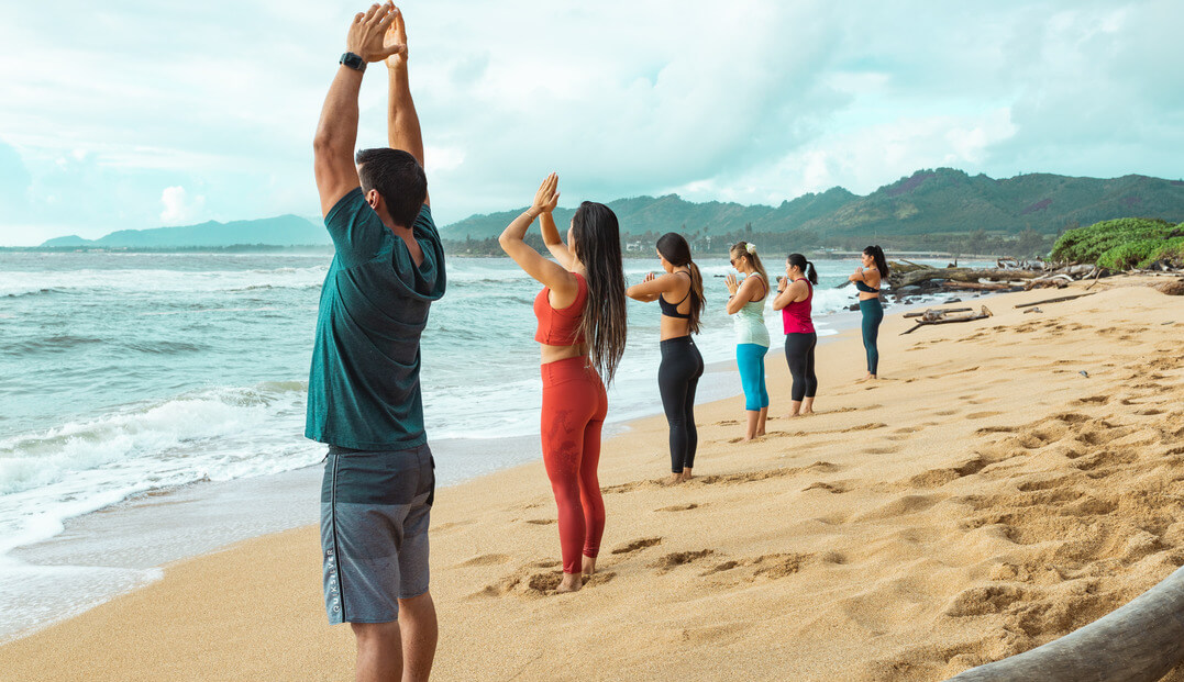 men and women facing the ocean doing yoga on the shoreline