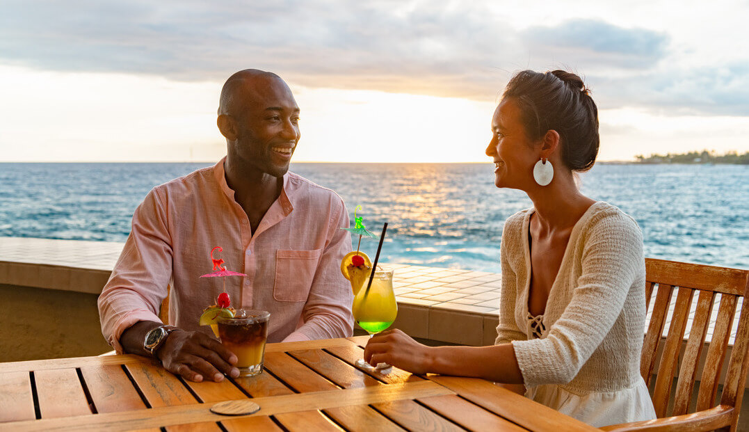 couple enjoying drinks during sunset with ocean in background 