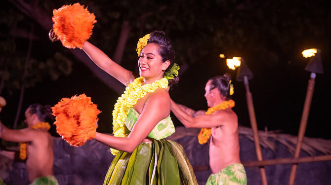woman with orange maracas in hand dancing in luau