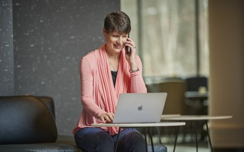 woman in pink cardigan on her phone and laptop