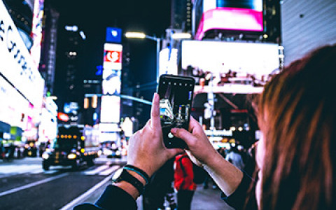 a woman taking a picture on her iphone of times square lit up at night