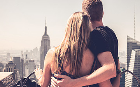 a man and woman with their arms around each other looking at the empire state building from a rooftop