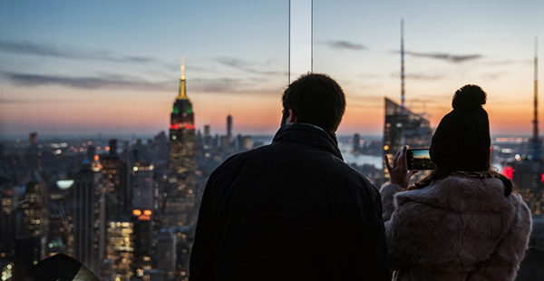 a man and woman standing on a rooftop building looking out over the new york city buildings at night