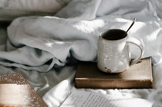 a coffee mug sitting on a wooden platter on a messy bed