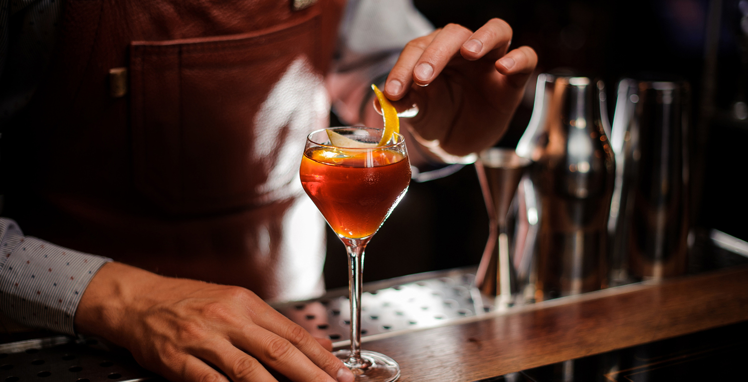 a bartender puts a lemon garnish in a cocktail drink