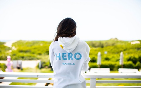 woman on a balcony wearing a hero beach club sweatshirt