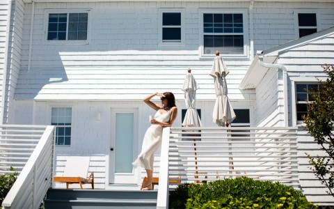 woman in a white dress standing on a porch leaning on the railing
