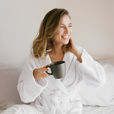 woman smiling in a robe holding a black mug