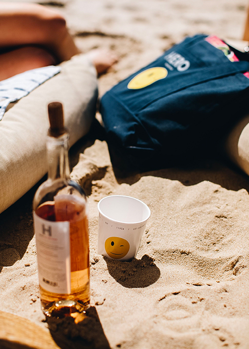 view of an alcohol bottle next to a hero beach club cup and bag in the sand
