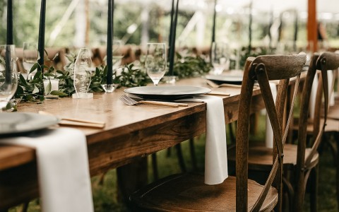 wooden table and chairs set up for dinner at a wedding reception
