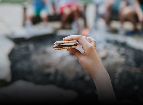 smore being held in a hand in front of a bonfire 