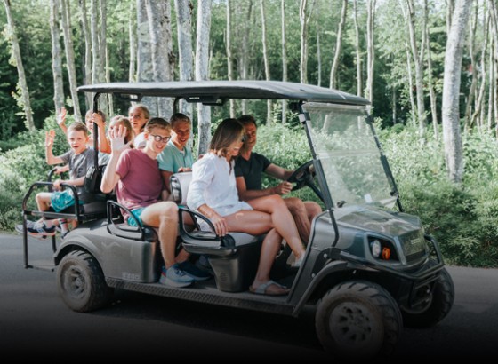 family with six kids sitting in a golf cart waving at the camera 