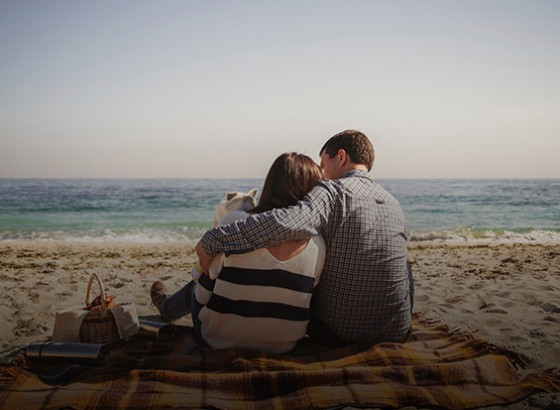 couple sitting together on a blanket having a picnic on the beach