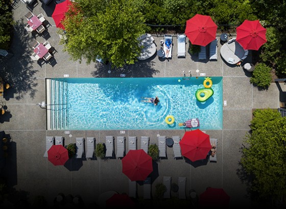 aerial image of adult pool with some pool floats and surrounding lounge seating and red umbrellas