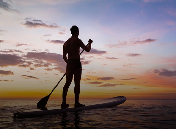 person standing on a paddle board in the ocean during sunset